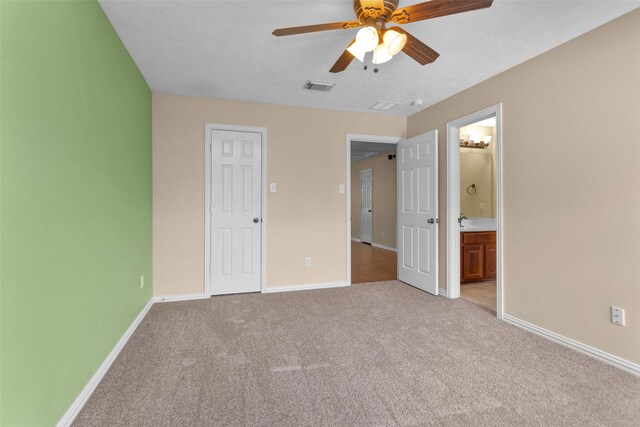 unfurnished bedroom featuring ceiling fan, light colored carpet, and ensuite bath