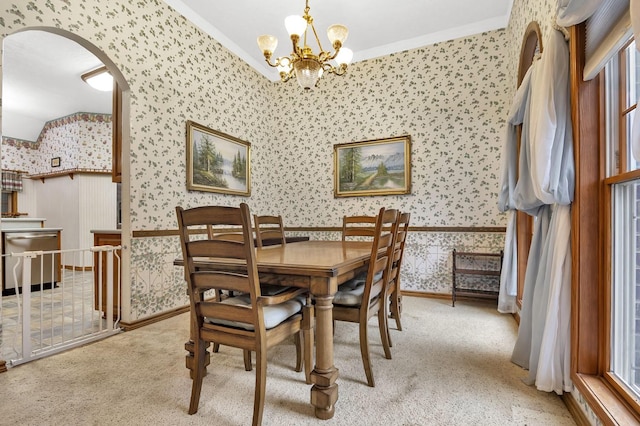 carpeted dining area featuring an inviting chandelier, a healthy amount of sunlight, lofted ceiling, and ornamental molding