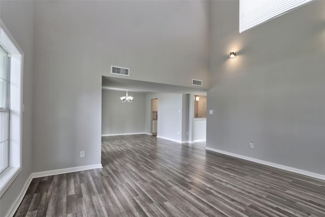 unfurnished living room with dark wood-type flooring, a high ceiling, and an inviting chandelier