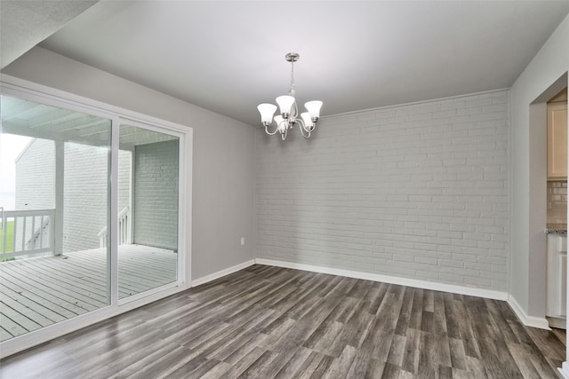 spare room with dark hardwood / wood-style flooring, an inviting chandelier, and brick wall