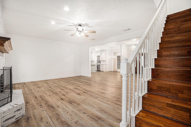 unfurnished living room featuring a textured ceiling, light hardwood / wood-style floors, and ceiling fan with notable chandelier