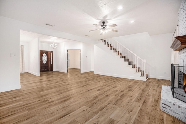 unfurnished living room featuring ceiling fan with notable chandelier, a textured ceiling, and light wood-type flooring