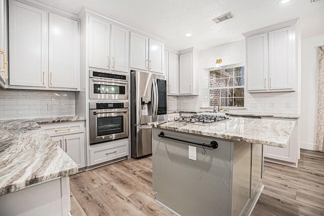 kitchen with light stone countertops, appliances with stainless steel finishes, backsplash, light hardwood / wood-style flooring, and white cabinets