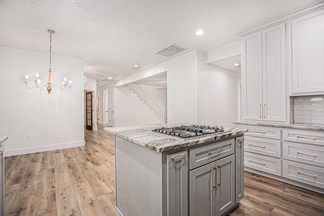 kitchen with tasteful backsplash, light stone counters, stainless steel gas stovetop, a kitchen island, and hardwood / wood-style flooring