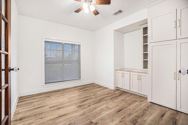 interior space featuring ceiling fan, light wood-type flooring, and a textured ceiling