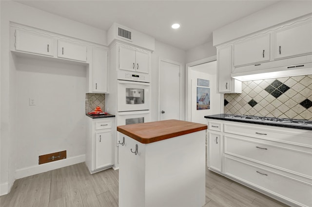 kitchen featuring light wood-type flooring, backsplash, double oven, white cabinets, and a kitchen island