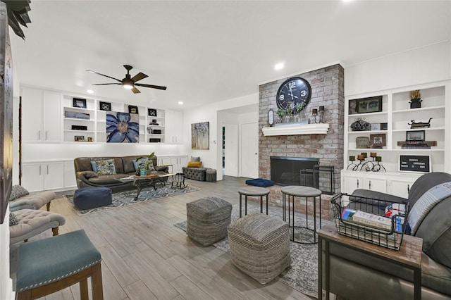 living room featuring hardwood / wood-style floors, a brick fireplace, ceiling fan, and built in shelves