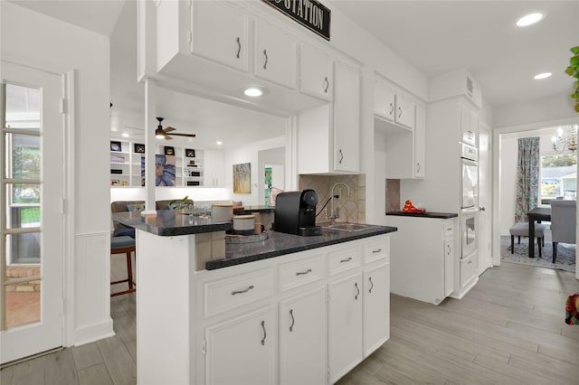 kitchen with white cabinets, a kitchen breakfast bar, sink, light hardwood / wood-style flooring, and kitchen peninsula