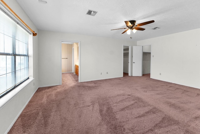 unfurnished bedroom featuring ceiling fan, a spacious closet, light carpet, and a textured ceiling