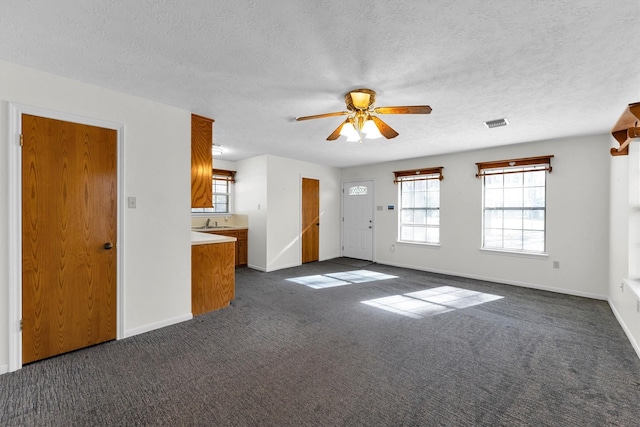 unfurnished living room with ceiling fan, sink, a textured ceiling, and dark carpet