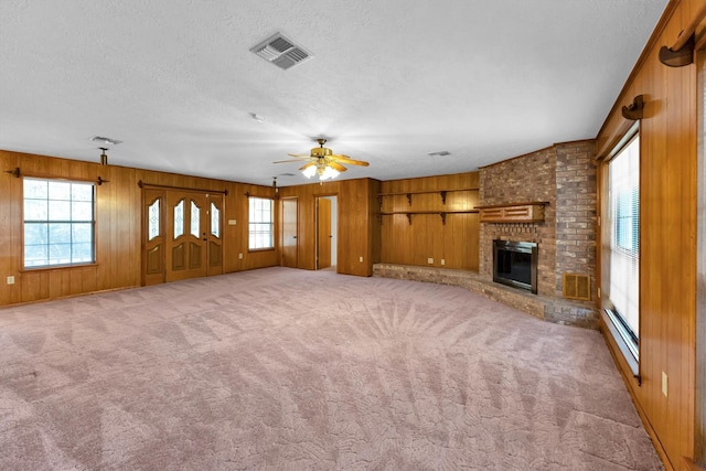 unfurnished living room with light colored carpet, wooden walls, a brick fireplace, and a textured ceiling