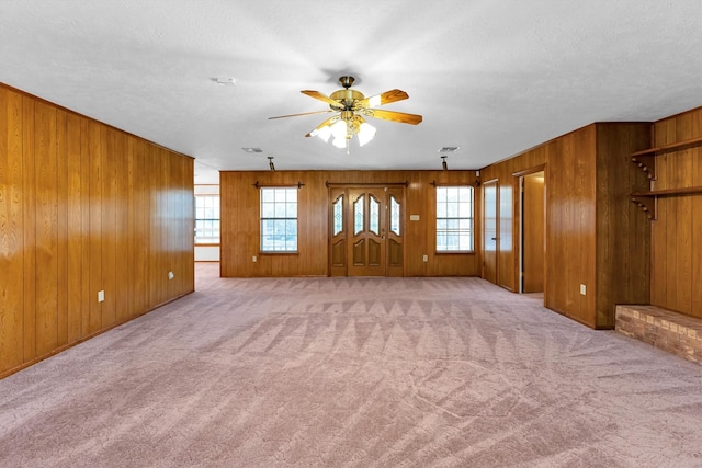 unfurnished living room with light colored carpet, a textured ceiling, ceiling fan, and wood walls