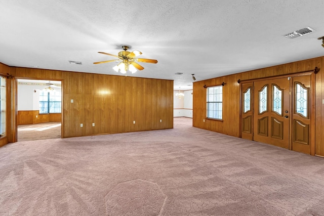 unfurnished living room with wooden walls, ceiling fan with notable chandelier, light carpet, and a textured ceiling