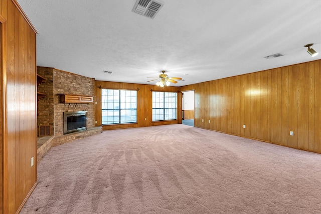 unfurnished living room with wood walls, carpet, ceiling fan, a brick fireplace, and a textured ceiling