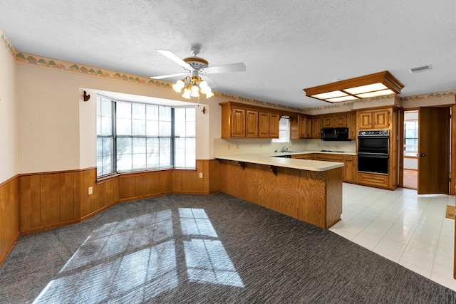 kitchen with kitchen peninsula, wood walls, ceiling fan, black appliances, and a textured ceiling