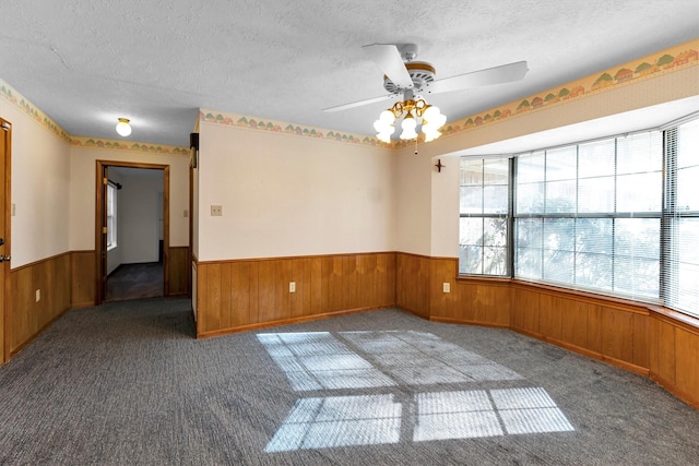 empty room with ceiling fan, dark colored carpet, a textured ceiling, and wood walls