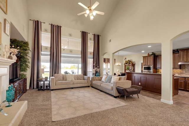 carpeted living room with high vaulted ceiling and ceiling fan with notable chandelier