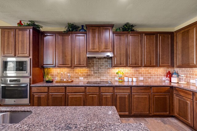 11411 Kings Point Blvd, Mont Belvieu, TX 77535 - kitchen with stainless steel appliances, under cabinet range hood, dark stone countertops, tasteful backsplash, and light stone finish floors