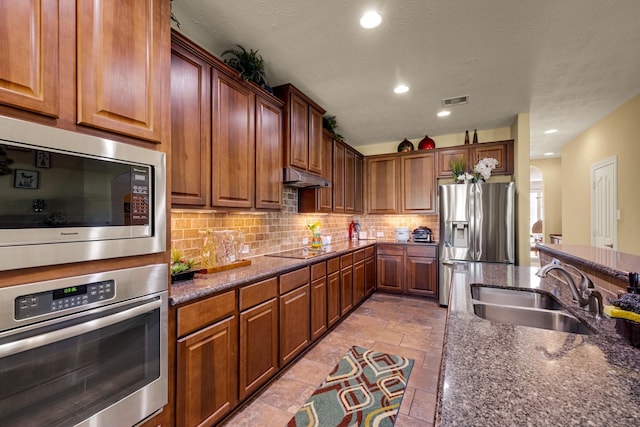 kitchen featuring backsplash, sink, dark stone countertops, a textured ceiling, and stainless steel appliances