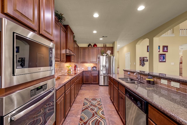 kitchen featuring stainless steel appliances, tasteful backsplash, dark stone counters, and sink