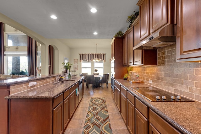 kitchen featuring custom exhaust hood, black electric cooktop, a kitchen island with sink, sink, and decorative light fixtures