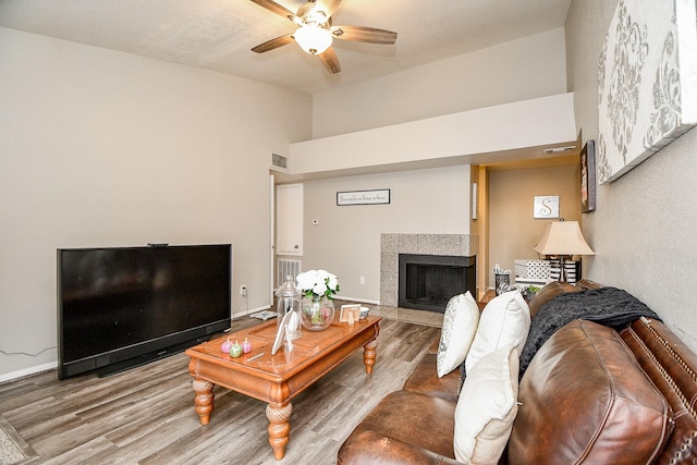 living room with hardwood / wood-style flooring, ceiling fan, and a tiled fireplace