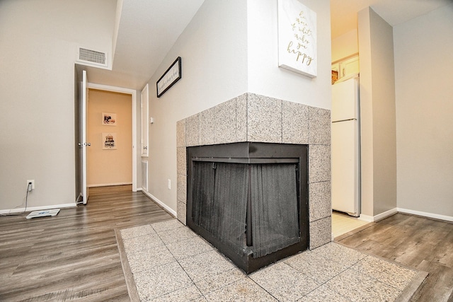 interior space featuring a tiled fireplace, wood-type flooring, and white refrigerator