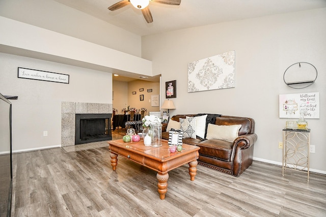 living room with ceiling fan, lofted ceiling, wood-type flooring, and a tiled fireplace