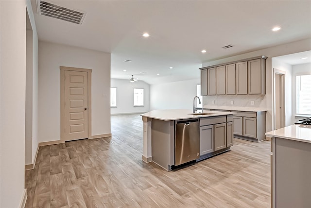 kitchen featuring light wood-type flooring, sink, dishwasher, gray cabinets, and an island with sink