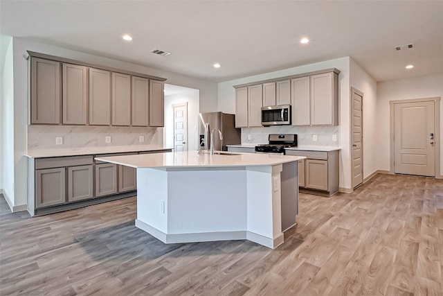 kitchen with gray cabinets, decorative backsplash, stainless steel appliances, and light wood-type flooring