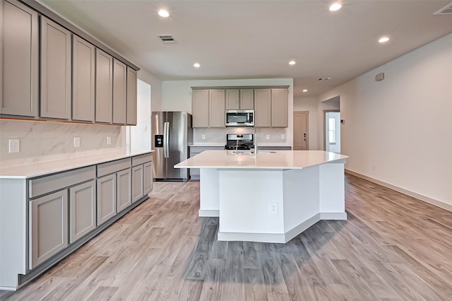 kitchen featuring gray cabinets, a kitchen island with sink, light hardwood / wood-style floors, and appliances with stainless steel finishes