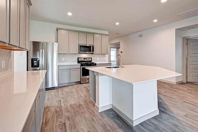 kitchen with appliances with stainless steel finishes, light wood-type flooring, gray cabinetry, sink, and a center island with sink