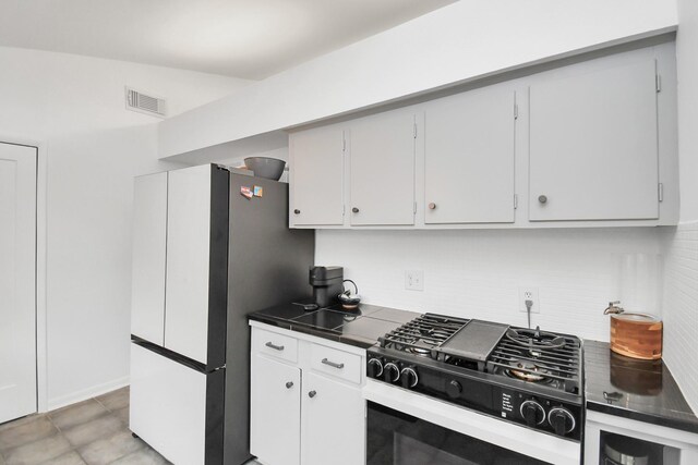 kitchen with stainless steel refrigerator, white cabinetry, stove, and tile counters