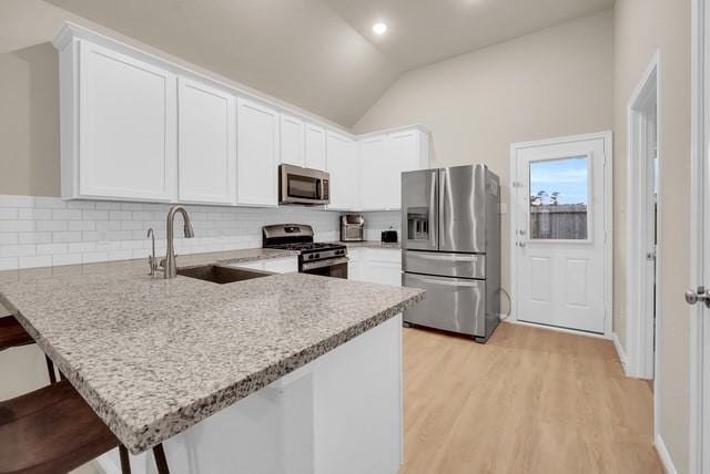 kitchen featuring a breakfast bar, sink, vaulted ceiling, kitchen peninsula, and stainless steel appliances