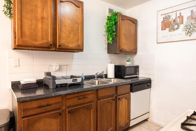 kitchen with tasteful backsplash, dishwasher, dark stone counters, and sink