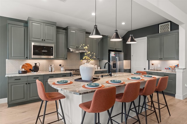 kitchen with sink, stainless steel appliances, backsplash, an island with sink, and light wood-type flooring