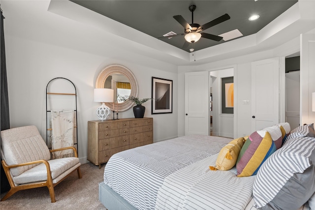 bedroom with ceiling fan, light colored carpet, and a tray ceiling