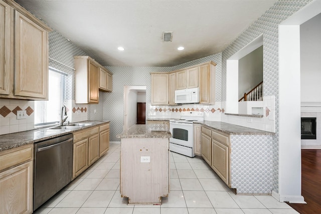 kitchen with light brown cabinetry, white appliances, sink, a center island, and a tiled fireplace