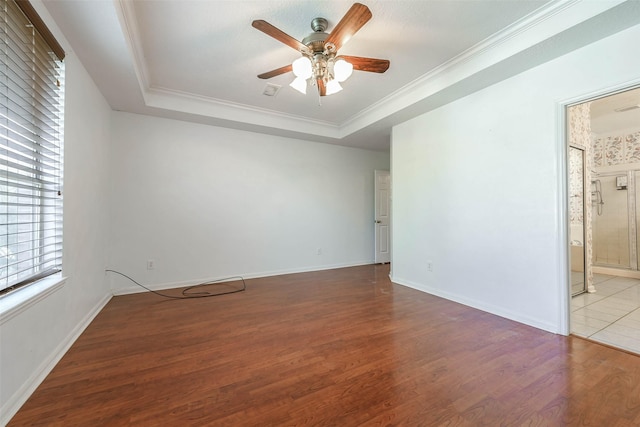 empty room with a tray ceiling, crown molding, ceiling fan, and hardwood / wood-style flooring