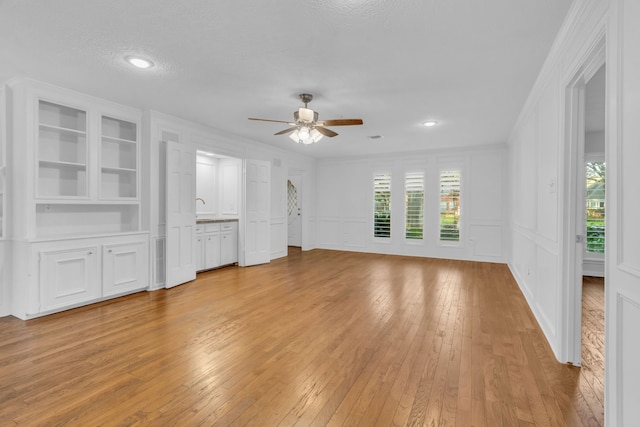 unfurnished living room with crown molding, ceiling fan, light hardwood / wood-style floors, a textured ceiling, and built in shelves