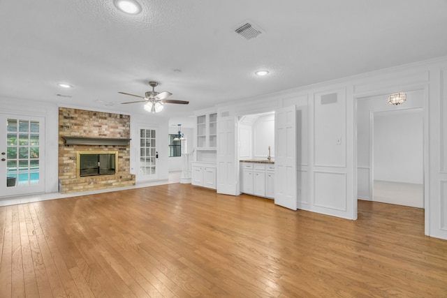 unfurnished living room featuring a brick fireplace, a textured ceiling, ornamental molding, ceiling fan, and light hardwood / wood-style floors