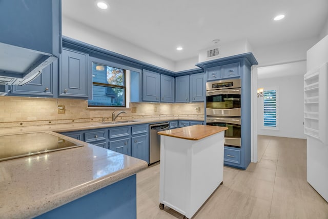 kitchen featuring sink, backsplash, stainless steel appliances, blue cabinets, and a kitchen island