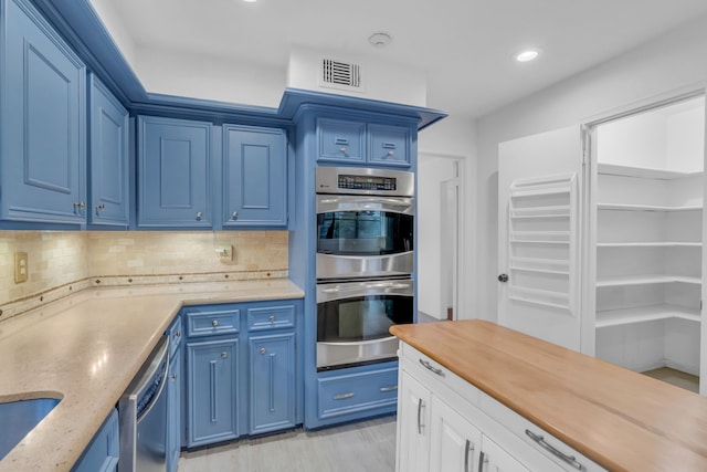 kitchen with stainless steel appliances, tasteful backsplash, blue cabinets, and butcher block countertops