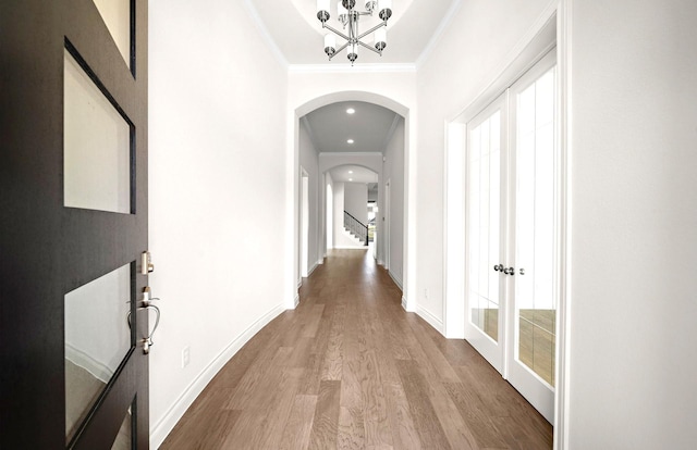 corridor featuring baseboards, arched walkways, wood finished floors, and a chandelier