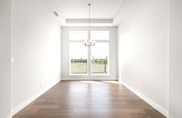 empty room with visible vents, wood finished floors, a raised ceiling, baseboards, and an inviting chandelier