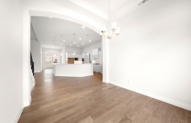 unfurnished living room with visible vents, arched walkways, light wood-type flooring, baseboards, and a notable chandelier