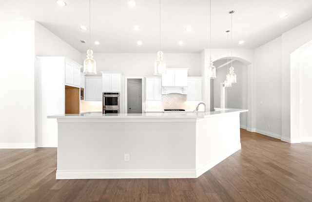 kitchen with a large island, stainless steel double oven, light countertops, white cabinets, and backsplash