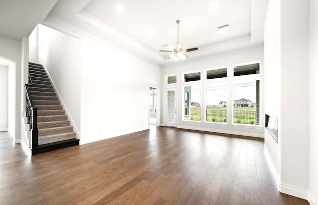 unfurnished living room featuring ceiling fan, stairway, a raised ceiling, visible vents, and hardwood / wood-style flooring