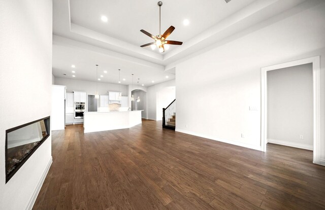 unfurnished living room with a ceiling fan, stairway, dark wood-type flooring, arched walkways, and a multi sided fireplace