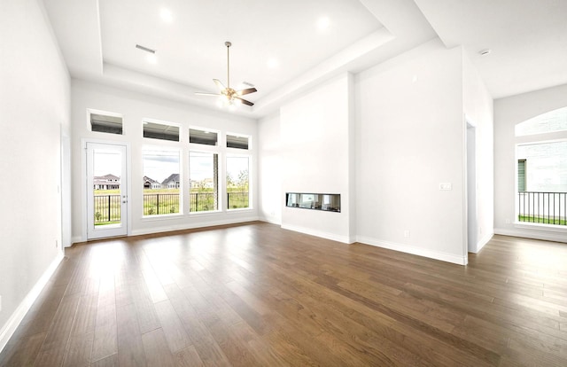 unfurnished living room featuring a raised ceiling, baseboards, a ceiling fan, and dark wood-style flooring